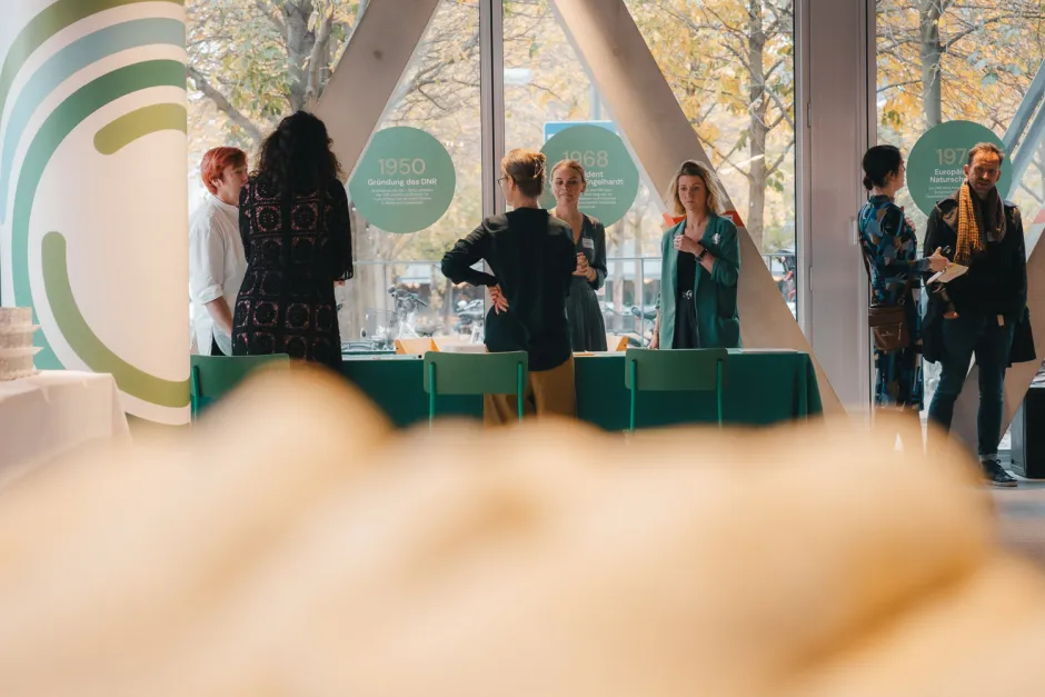 Blick auf Personen und die Ausstellung über 75 Jahre DNR (Chronikelemente als große runde Sticker an den SCheiben, die jeweils die Ereignisse einzelner Jahre kurz zusammenfassen)